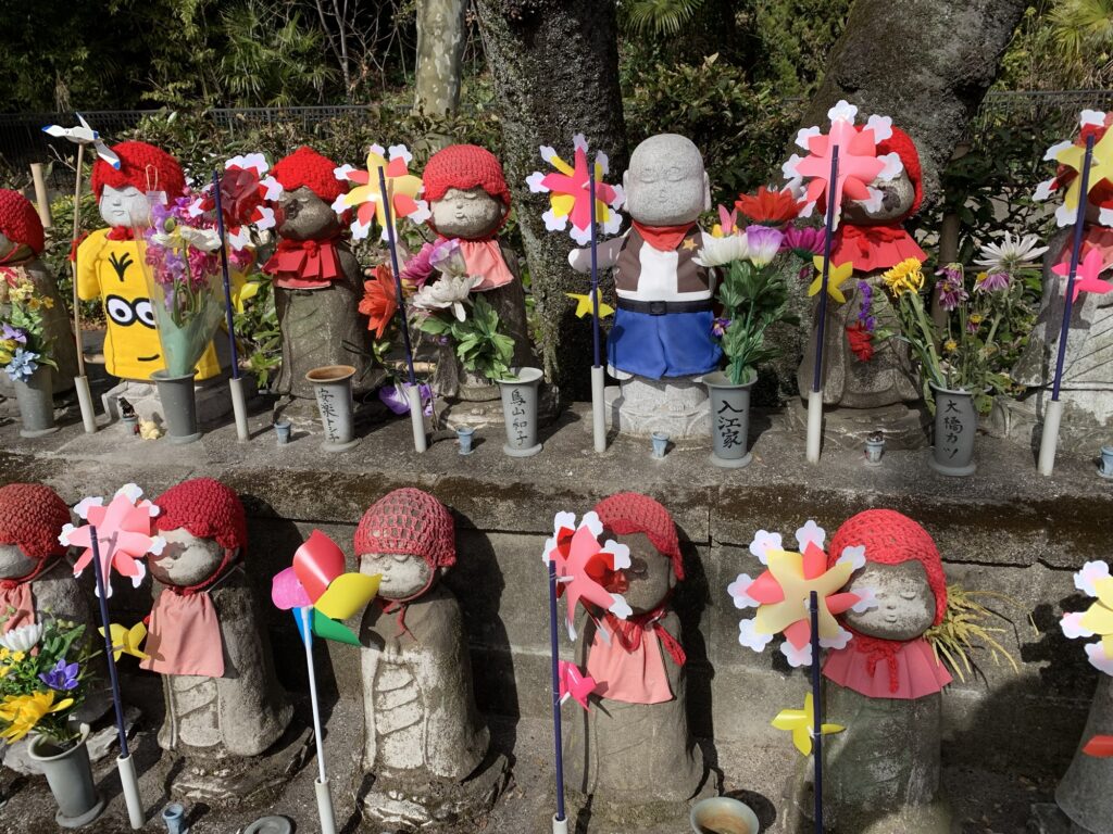 Statuer af babyer pyntet med blomster og vindfangere foran et tempel i tokyo