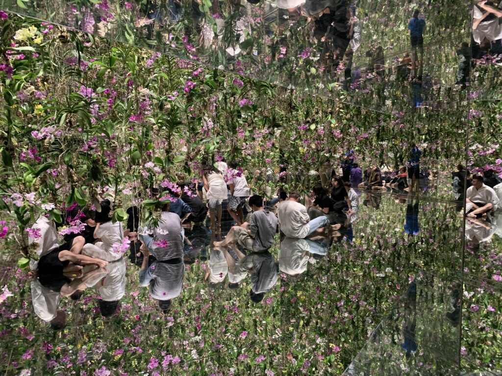 Turister der sidder på et spejlguld og tager billeder af svævende blomster, fra Teamlab Borderless i Tokyo.